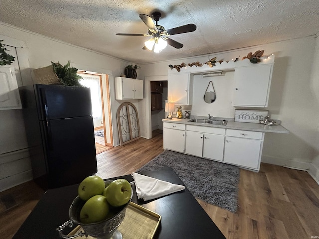 kitchen with wood finished floors, freestanding refrigerator, a textured ceiling, white cabinetry, and a sink