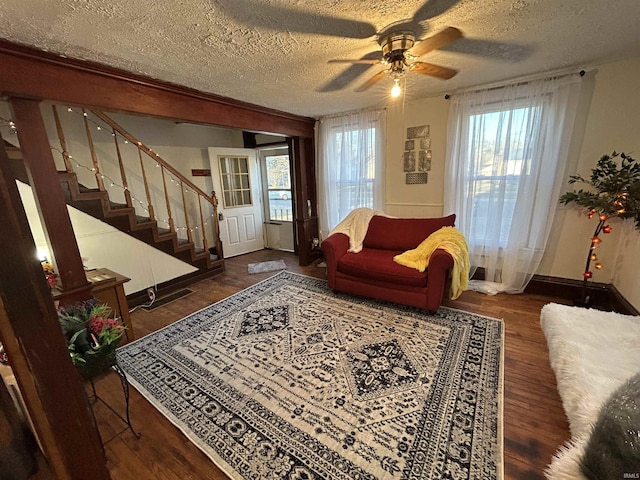 living room with stairs, a textured ceiling, baseboards, and wood finished floors