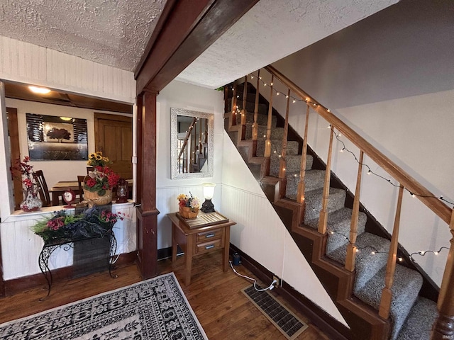 stairs with a textured ceiling, wainscoting, wood finished floors, and visible vents