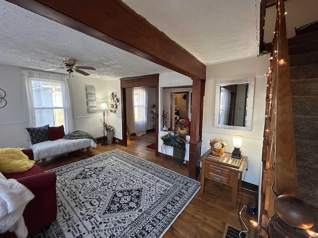 living room featuring a textured ceiling, ceiling fan, wood finished floors, visible vents, and beamed ceiling