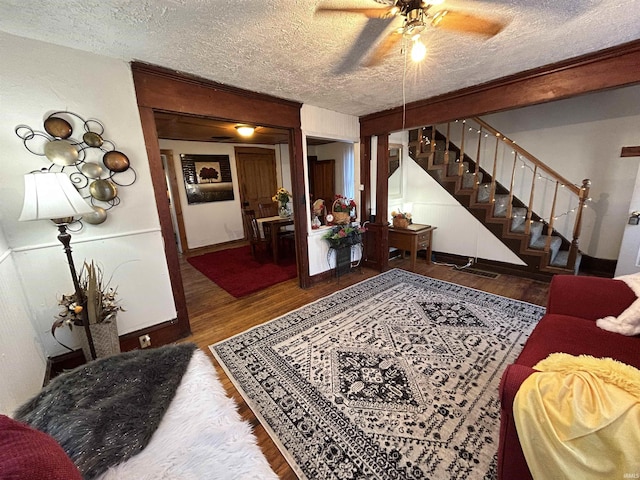 living area featuring a textured ceiling, ceiling fan, wood finished floors, and stairs