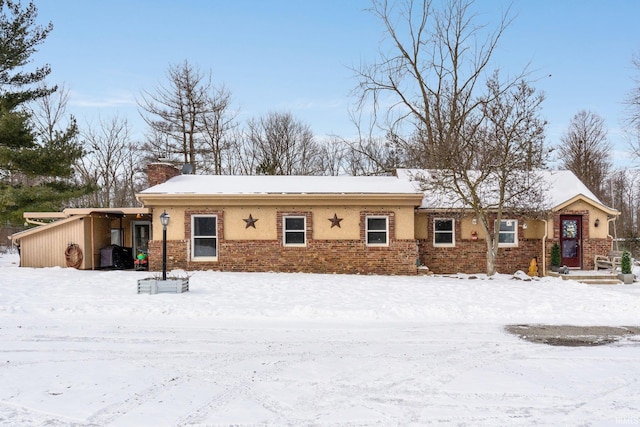 snow covered rear of property featuring an attached carport and brick siding