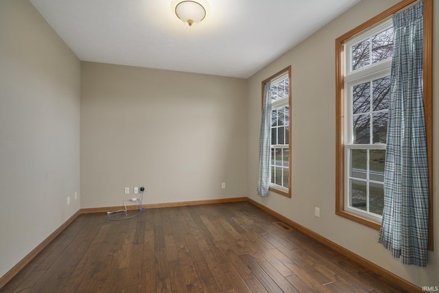 unfurnished room with dark wood-style floors, visible vents, and baseboards