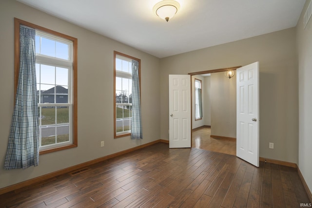 empty room with dark wood-style flooring, visible vents, and baseboards