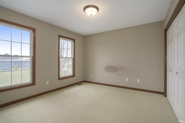 spare room with a wealth of natural light, light colored carpet, visible vents, and baseboards