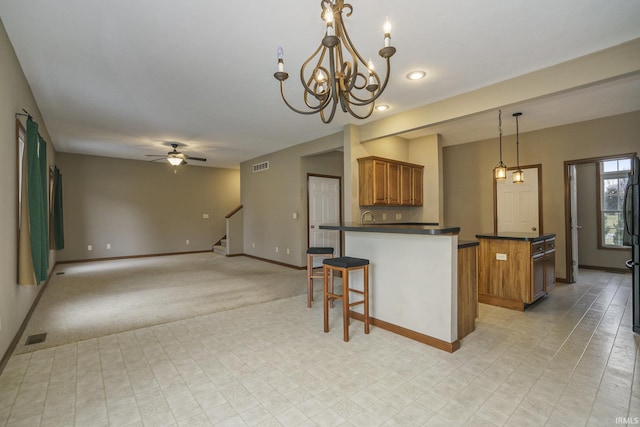 kitchen with brown cabinetry, dark countertops, visible vents, and a peninsula