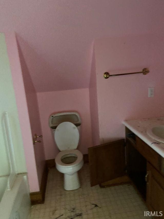 bathroom featuring baseboards, vaulted ceiling, vanity, and toilet