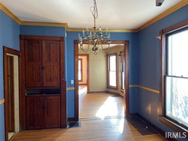 unfurnished dining area with plenty of natural light, crown molding, baseboards, and wood finished floors