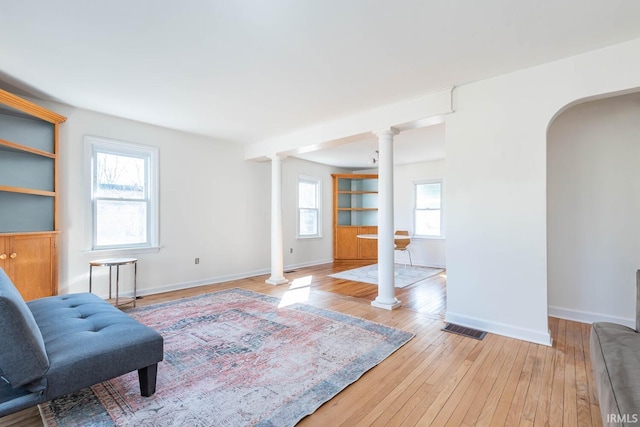 living area with visible vents, wood-type flooring, decorative columns, and plenty of natural light