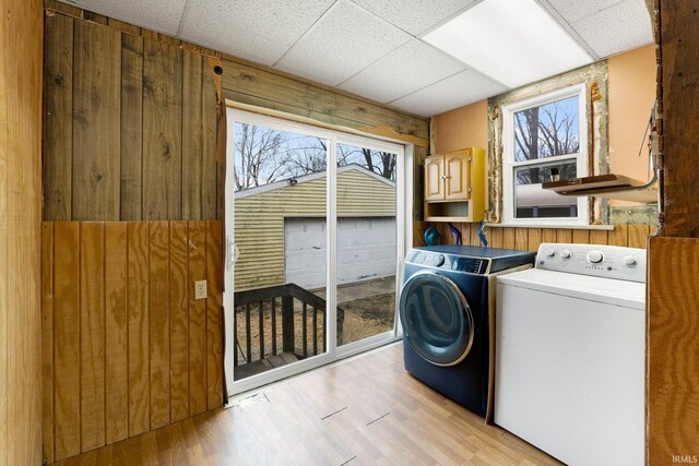 laundry area featuring cabinet space, wood walls, light wood-style flooring, and separate washer and dryer