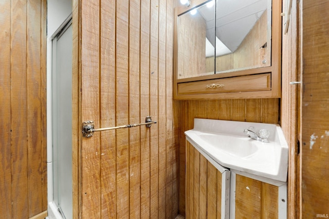 bathroom featuring a stall shower, a sink, and wooden walls