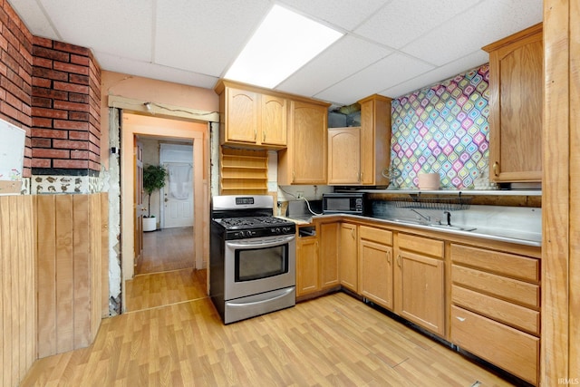 kitchen featuring black microwave, light wood-style flooring, a sink, stainless steel gas stove, and light brown cabinetry