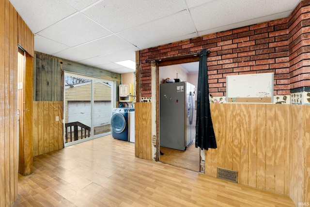 spare room featuring a paneled ceiling, wood walls, wood finished floors, visible vents, and washer / clothes dryer