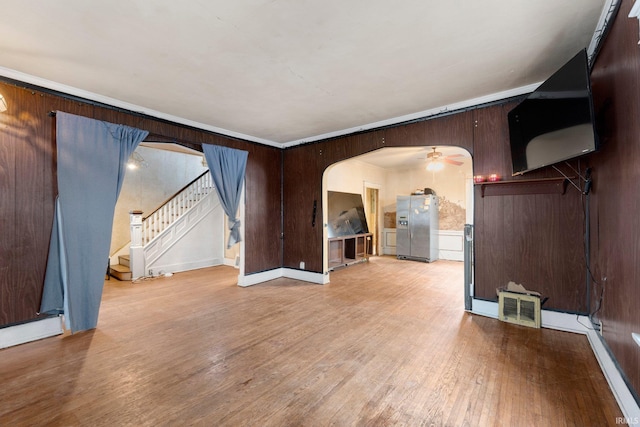 unfurnished living room featuring arched walkways, visible vents, wooden walls, wood finished floors, and stairs