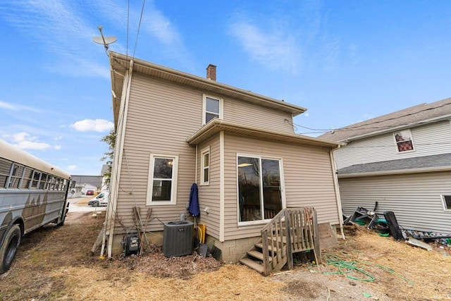 rear view of house with central air condition unit and a chimney