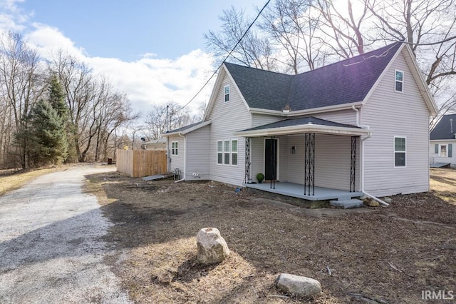 view of front of home featuring covered porch, roof with shingles, fence, and driveway