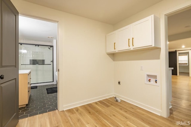 clothes washing area with cabinet space, a barn door, baseboards, hookup for a washing machine, and light wood-type flooring