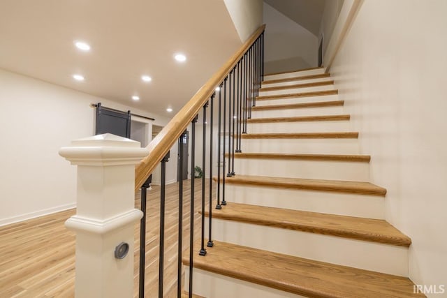 staircase with a barn door, wood finished floors, and recessed lighting