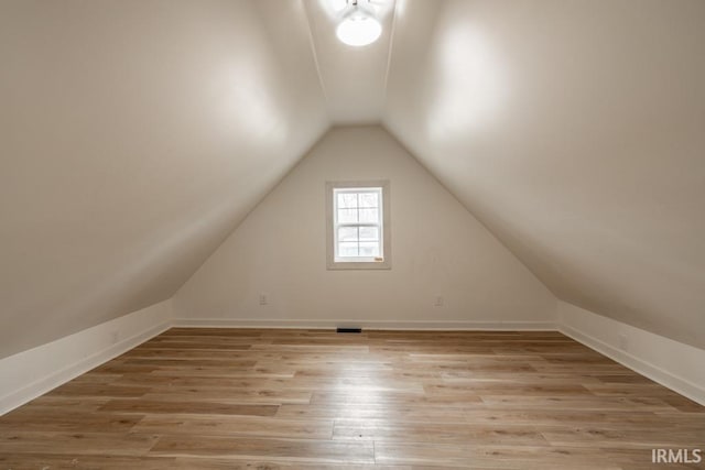 additional living space with light wood-style flooring, baseboards, and vaulted ceiling