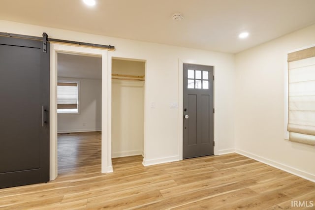 entrance foyer with a barn door, recessed lighting, light wood-style flooring, and baseboards