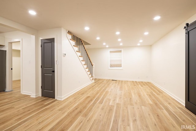 finished basement with stairs, recessed lighting, light wood-style flooring, and a barn door