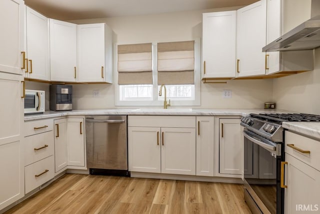 kitchen with stainless steel appliances, light countertops, light wood-style flooring, a sink, and wall chimney exhaust hood