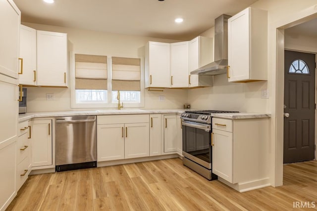 kitchen with wall chimney exhaust hood, light wood-style flooring, appliances with stainless steel finishes, light countertops, and a sink