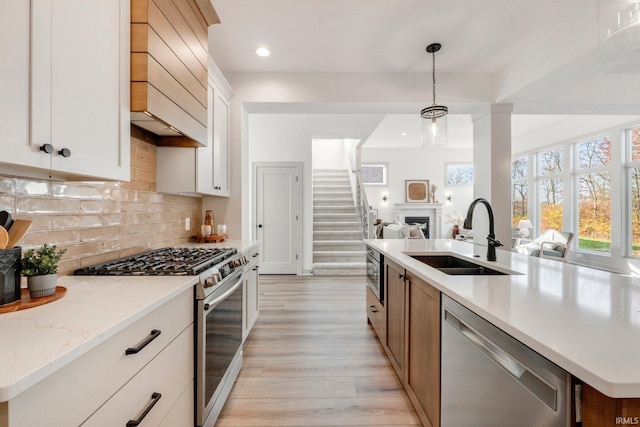 kitchen with tasteful backsplash, appliances with stainless steel finishes, open floor plan, light wood-style floors, and a sink