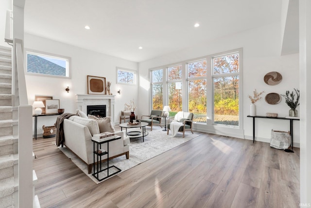 living room featuring a glass covered fireplace, stairway, recessed lighting, and wood finished floors