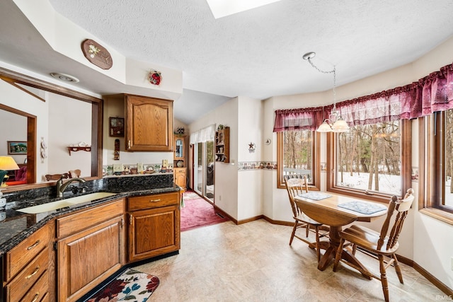 kitchen with brown cabinets, a sink, a textured ceiling, and baseboards