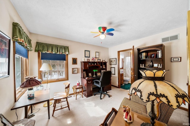 carpeted home office featuring a textured ceiling, baseboards, visible vents, and a ceiling fan