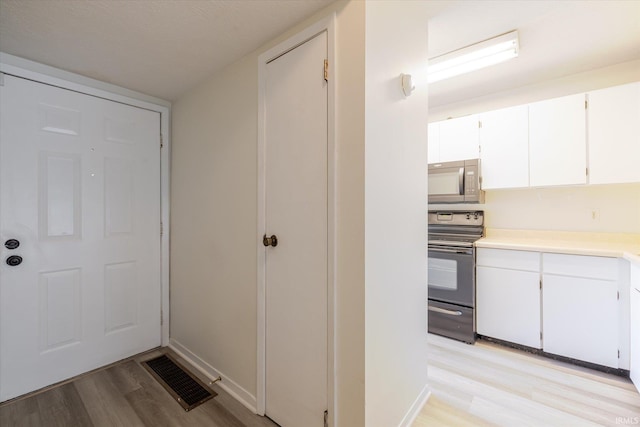 kitchen featuring stainless steel microwave, black range with electric stovetop, visible vents, light wood-style floors, and white cabinetry