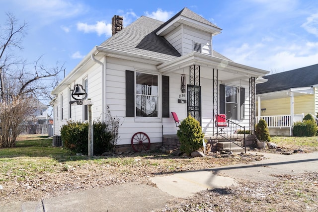 view of front of home with covered porch, roof with shingles, and a chimney