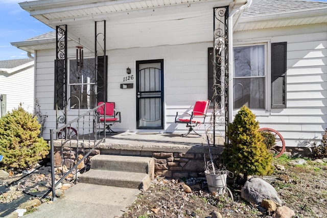 doorway to property featuring covered porch and roof with shingles