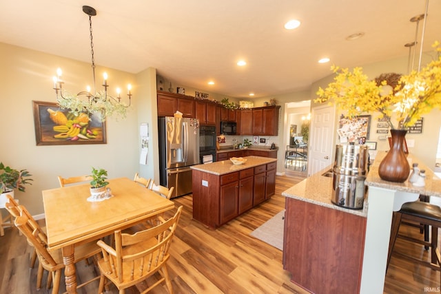 kitchen with light wood-style flooring, a kitchen island, black appliances, a notable chandelier, and recessed lighting