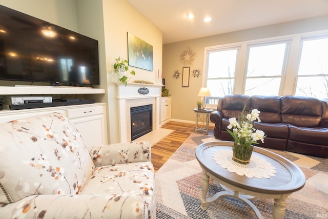 living area featuring a fireplace with flush hearth, baseboards, light wood-style flooring, and recessed lighting