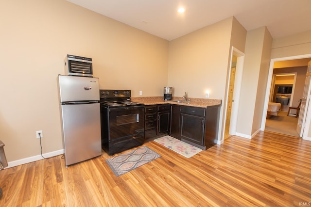 kitchen with light stone counters, light wood finished floors, freestanding refrigerator, a sink, and black range with electric cooktop