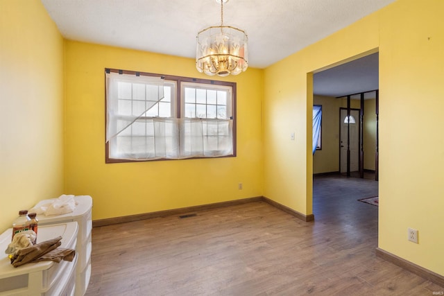 empty room featuring a chandelier, visible vents, baseboards, and wood finished floors