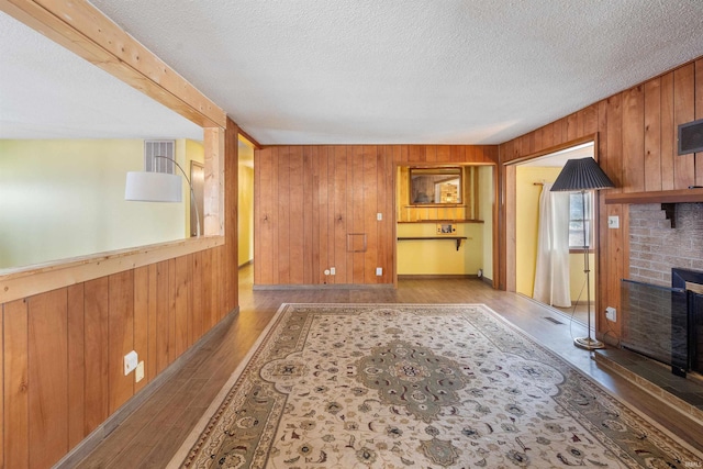 unfurnished living room with a textured ceiling, a brick fireplace, wood finished floors, and wooden walls