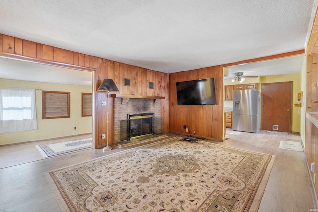 living room featuring a textured ceiling, wooden walls, visible vents, a brick fireplace, and light wood finished floors