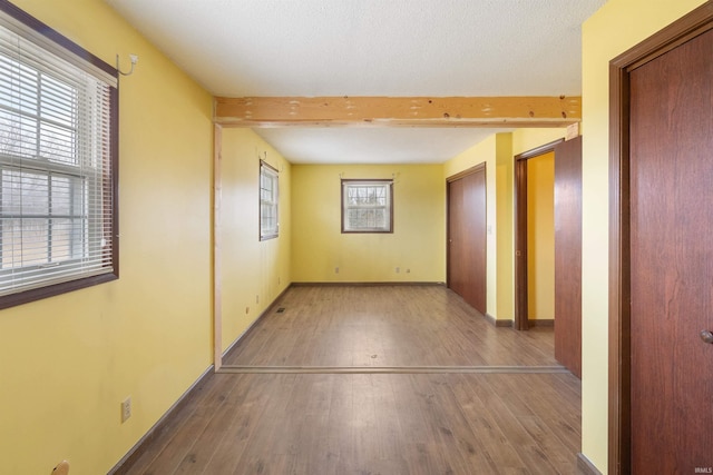 empty room featuring hardwood / wood-style flooring, baseboards, and beam ceiling