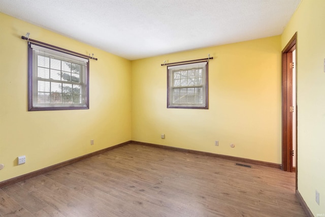 unfurnished room with wood finished floors, visible vents, and baseboards