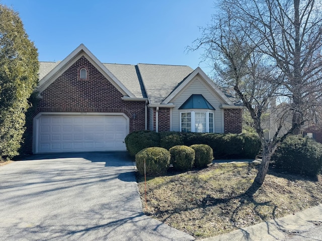 ranch-style home featuring brick siding, driveway, an attached garage, and roof with shingles