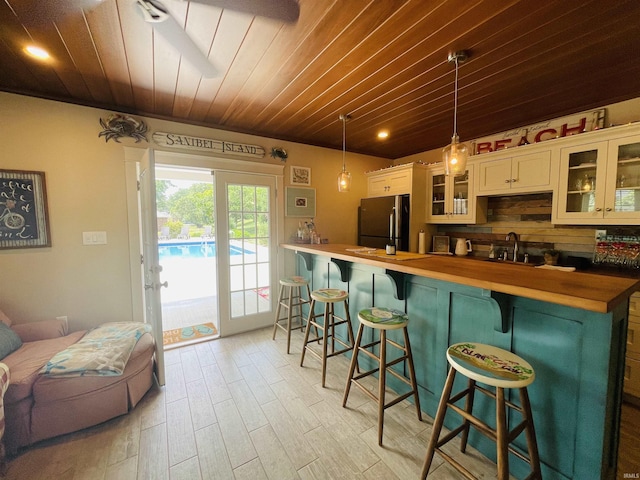 kitchen featuring a sink, wood ceiling, a kitchen breakfast bar, wooden counters, and freestanding refrigerator