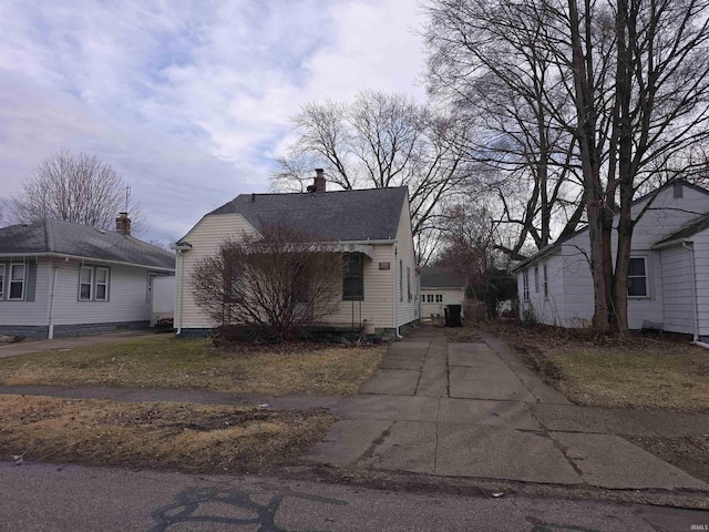 view of front facade featuring driveway, roof with shingles, and a chimney