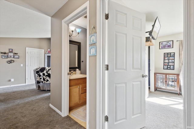 corridor with lofted ceiling, baseboards, a sink, and light colored carpet