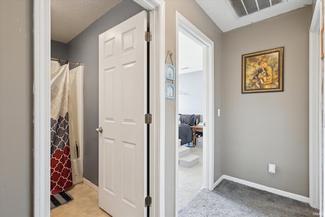 hall featuring light colored carpet, visible vents, a textured ceiling, and baseboards