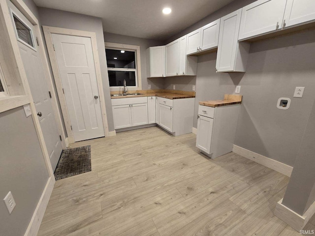 kitchen featuring baseboards, white cabinets, light wood-style flooring, a sink, and recessed lighting