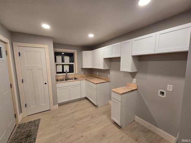 kitchen featuring light wood finished floors, baseboards, white cabinets, a sink, and recessed lighting