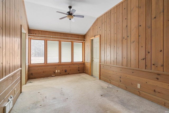 carpeted spare room featuring ceiling fan, wooden walls, and vaulted ceiling